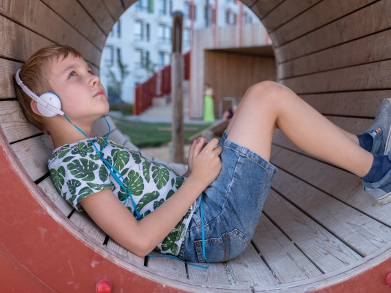 Boy sitting in a playground tube wearing headphones