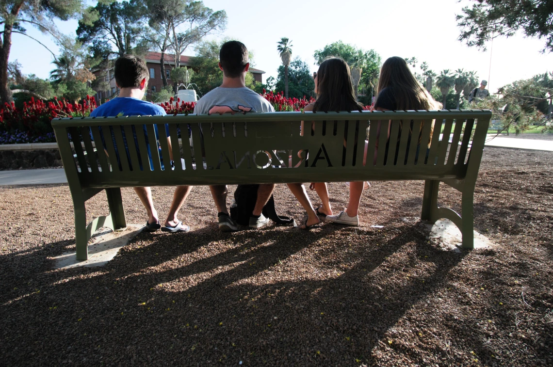 Students sitting on a bench facing the Old Main fountain