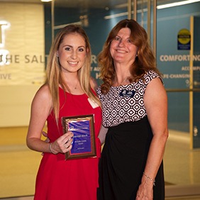 Two women posing for photo with an award plaque.