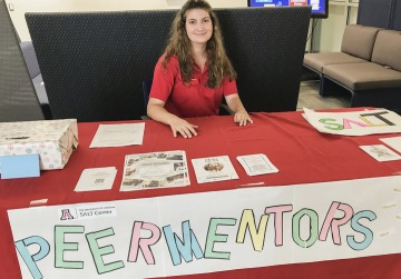 Olivia Broderson sitting in front of a Peer Mentor table