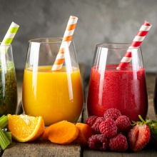 Colorful smoothies in glasses surrounded by fruits and vegetables