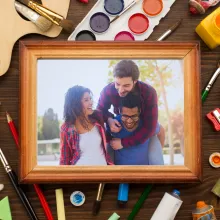 Table with crafts spread all over and a picture frame with a photo of 3 people in side.