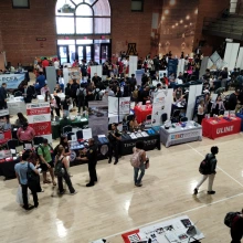 A college fair in a large hall filled with tables and banners and people visiting 